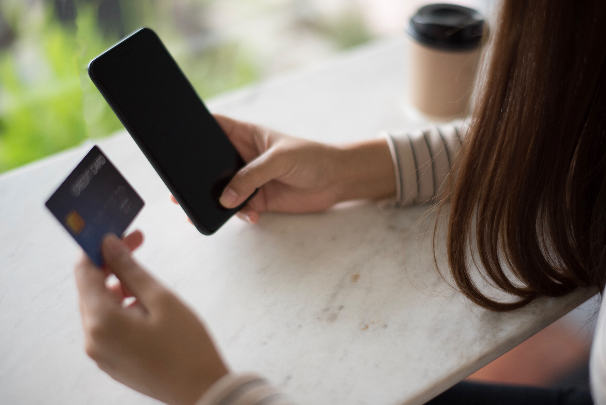 Closed up and focus on hand of young woman using a smartphone and other hand hold a credit card which is shopping online and sitting on table near big mirror at cafe. online payment concept. Closed up and focus on hand of young woman using a smartphone and other hand hold a credit card which is shopping online and sitting on table near big mirror at cafe. online payment concept.
